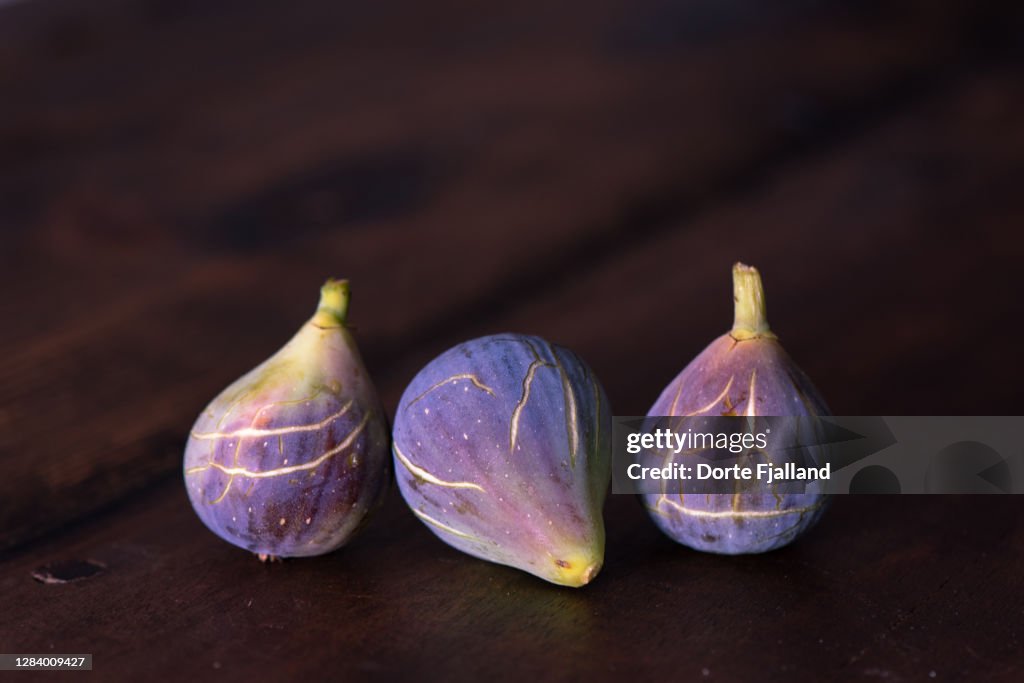 Three purple, ripe figs on a dark background