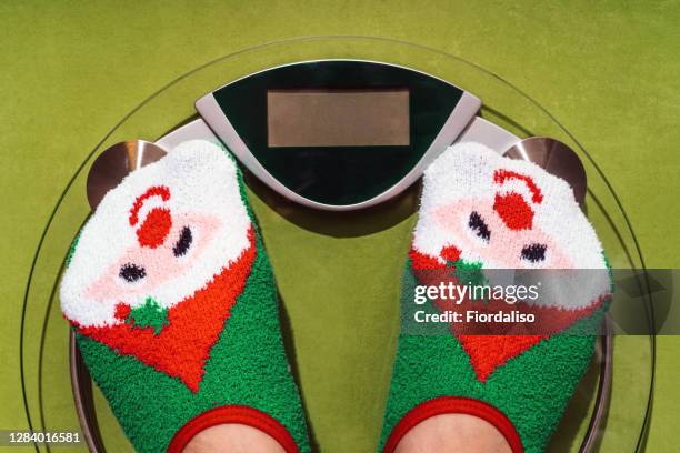 woman standing on the scales in christmas fun red green socks with snowman background. the problem of excess weight gained during the holiday new year - national diet of japan stock pictures, royalty-free photos & images