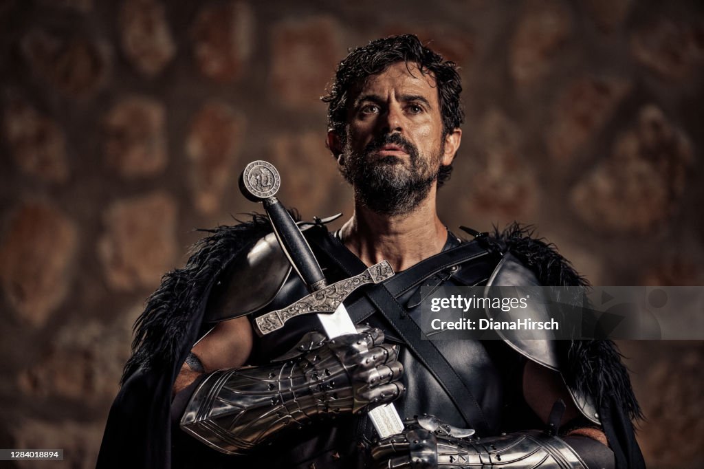 Devout mature fantasy medieval knight holding his sword in front of him while he is praying