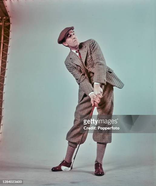Male model, wearing a tweed checked jacket with matching plus fours trousers, flat cap and brown brogue shoes typical of 1930's dress, poses with a...