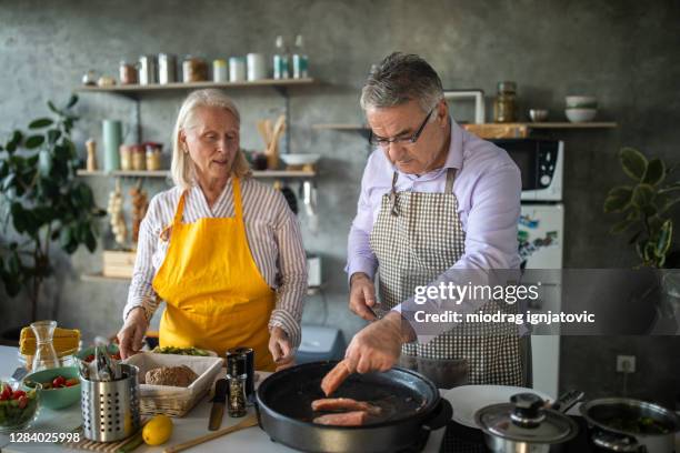 senior couple preparing healthy meal together at home - cooking fish stock pictures, royalty-free photos & images