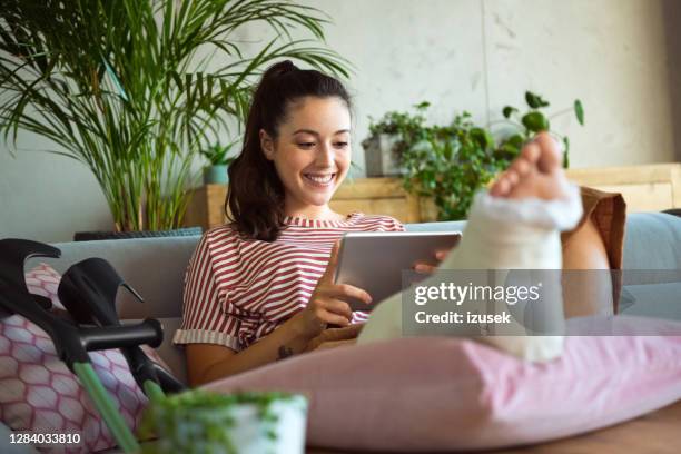 cheerful young woman with broken leg at home - broken leg stock pictures, royalty-free photos & images