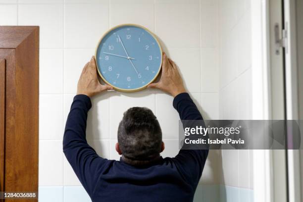 rear view of man fixing clock on wall - time of day stock pictures, royalty-free photos & images