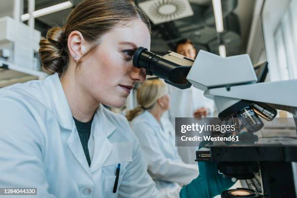 assistant analyzing human brain microscope slide while sitting with scientist in background at laboratory - cientifico con microscopio fotografías e imágenes de stock