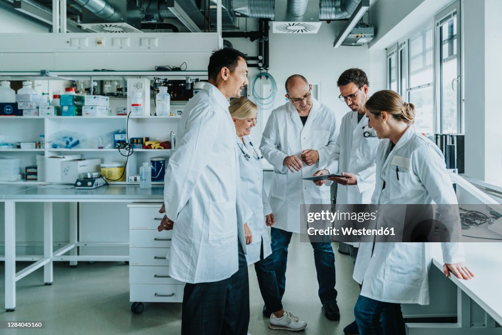 Team of scientist with digital tablet working together while standing at laboratory