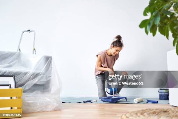 smiling young woman pouring paint in paint tray while kneeling at home - making painting stock-fotos und bilder