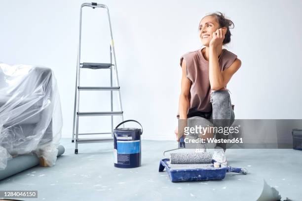 young woman head in hands holding paint roller in paint tray while crouching at home - holding paint roller stock pictures, royalty-free photos & images