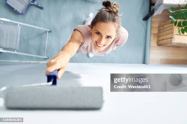 smiling young woman painting wall with paint roller while standing at home - konstmateriel bildbanksfoton och bilder