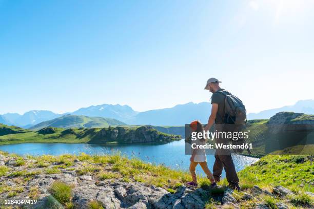 father and daughter walking on meadow during sunny day - mountain side stock pictures, royalty-free photos & images