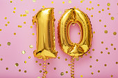 10 air balloon numbers on pink background. 10 k gold foil balloons with confetti. Birthday party flat lay with copy space