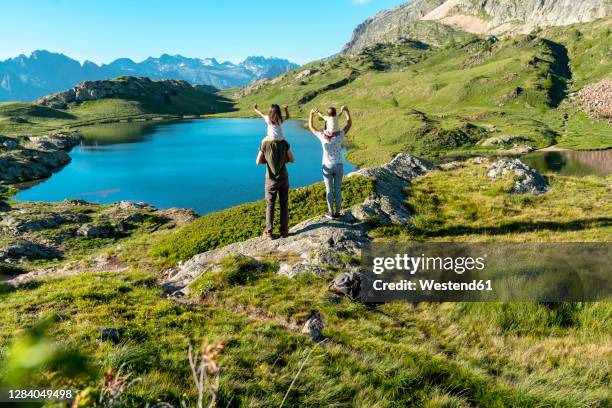 mother and father carrying daughters on shoulders looking at view while standing during sunny day - alpe d'huez stock pictures, royalty-free photos & images