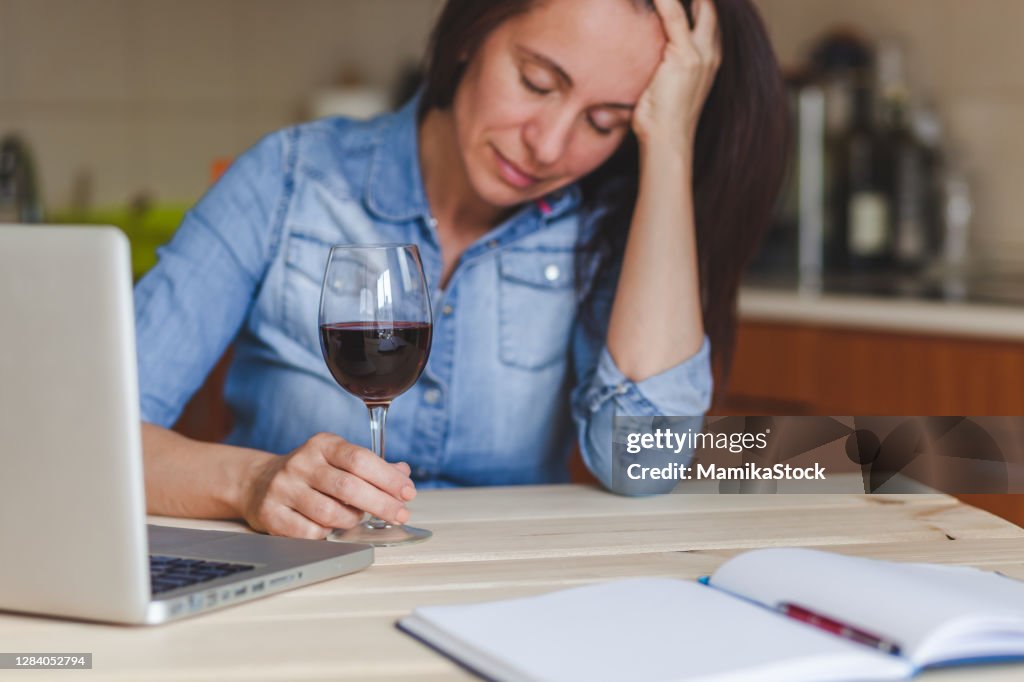 Depressed woman drinking red wine at home.