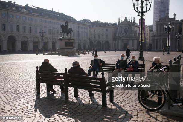 People wearing protective masks sit on benches at Piazza San Carlo during the last day before new lockdown measures for the Piedmont Region on...