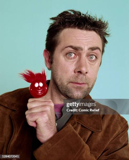 Irish stand-up comedian, Sean Hughes poses in the studio with a big hair do red nose on his thumb for Red Nose Day 2003.