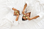 Black Mom And Daughter In Bathrobes Lying With Cucumber Slices On Eyes