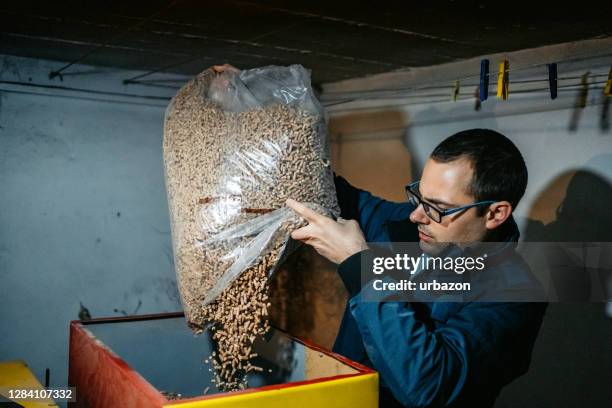 mann gießt pellets in pelletskessel - granulat stock-fotos und bilder