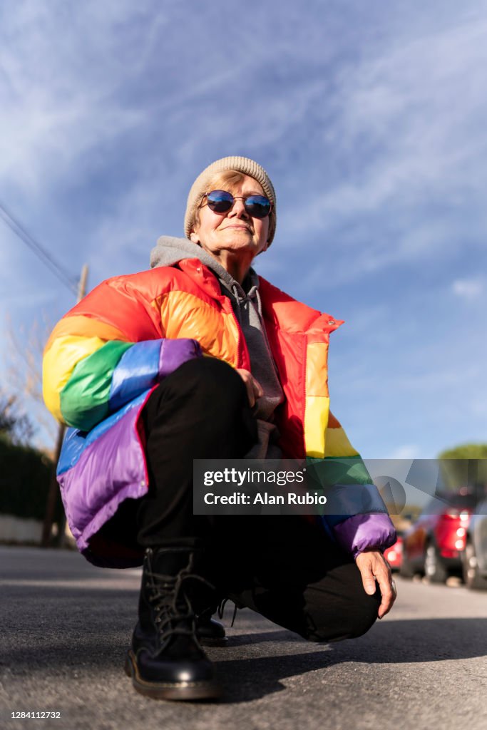 Modern grandmother in rainbow coat posing in the middle of the street.