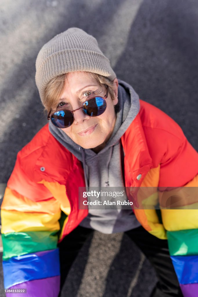 Grandmother in rainbow coat smiling in the middle of the street.