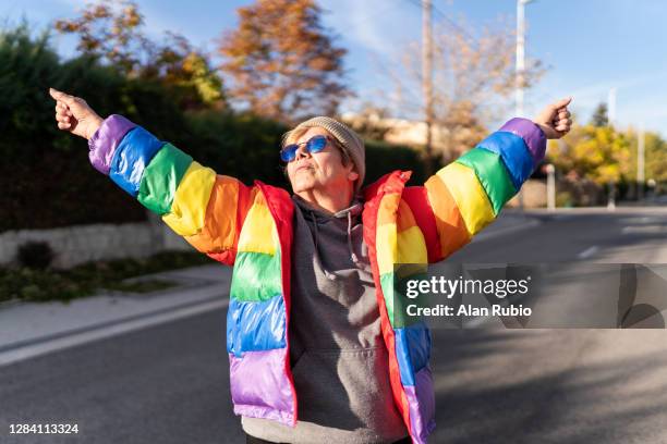 modern grandmother in rainbow coat posing in the middle of the street. - regenbogenfahne stock-fotos und bilder