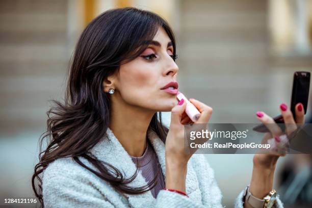 beautiful mid adult woman holding red lipstic and doing quick makeup on the city street - woman lipstick stock pictures, royalty-free photos & images