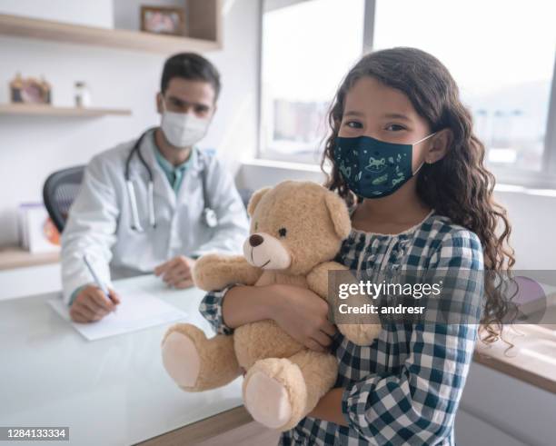 menina usando uma máscara facial em uma consulta médica enquanto segurava um ursinho de pelúcia - mama bear - fotografias e filmes do acervo