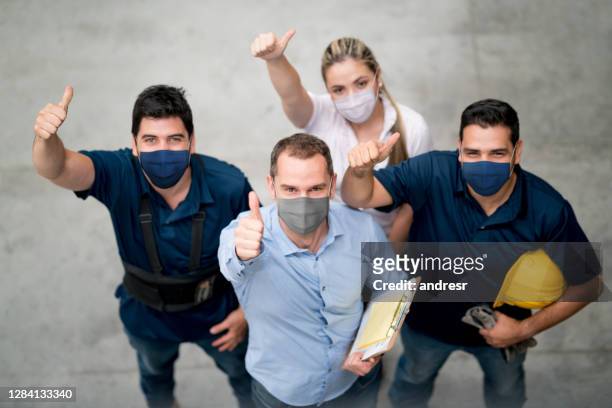 group of workers at a warehouse wearing facemasks and showing their with thumbs up - biosecurity stock pictures, royalty-free photos & images