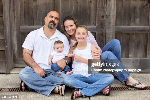a young family sitting in front of a wooden door - mesma roupa imagens e fotografias de stock