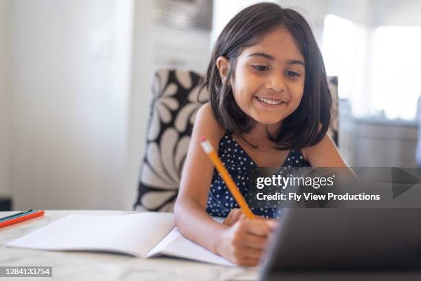 nettes grundschulalter mädchen mit laptop-computer, während der besuch der schule online - hausaufgaben stock-fotos und bilder