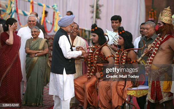 Prime Minister Manmohan Singh holding a lamp prepares to apply a vermillion mark on the forehead of actors dressed as Hindu God Rama during the...