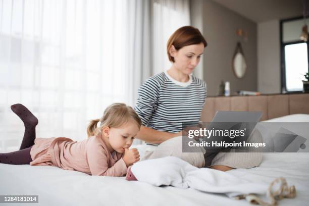 working mother using laptop and daughter with smartphone in bedroom, home office with kids concept. - thumb sucking stock pictures, royalty-free photos & images
