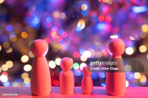 wooden figurines represent family with two small children.  in the background and out of focus, there is a christmas tree decorated with colorful flickering lights, garlands and christmas baubles. camera pan movement. - in law relations stockfoto's en -beelden