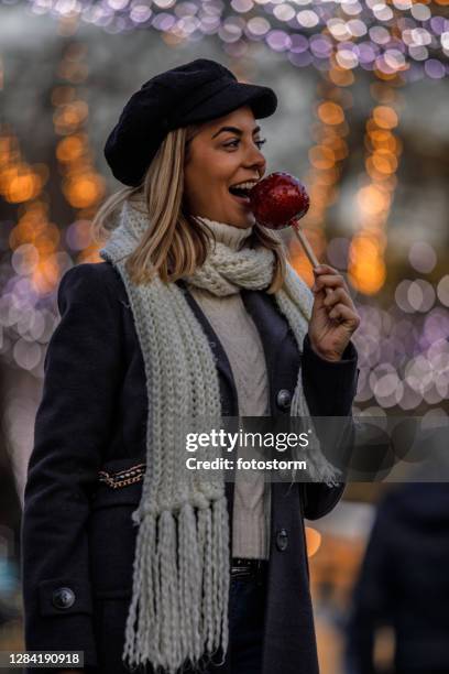 gelukkige blonde die een beet van een appel van het suikergoed van kerstmis neemt - blond women happy eating stockfoto's en -beelden