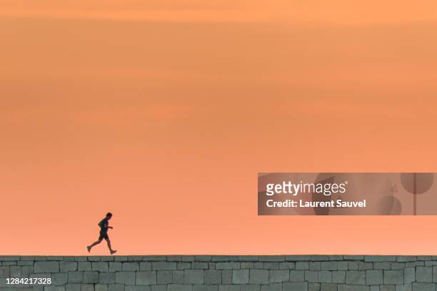 silhouette of a running man at sunset under a beautiful pink orange sky - laurent sauvel photos et images de collection