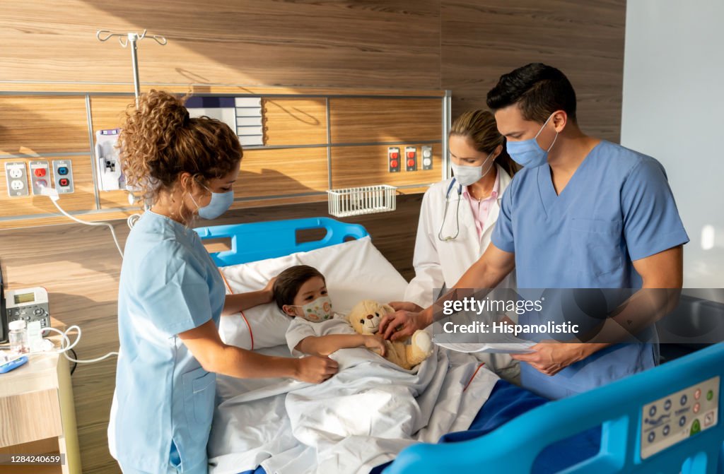 Junge im Krankenhaus umgeben von Medizinischem Personal und tragen Gesichtsmasken während der Pandemie