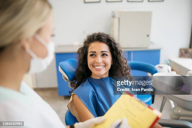 attraktive junge kaukasische frau im gespräch mit ihrem zahnarzt - a dentist stock-fotos und bilder