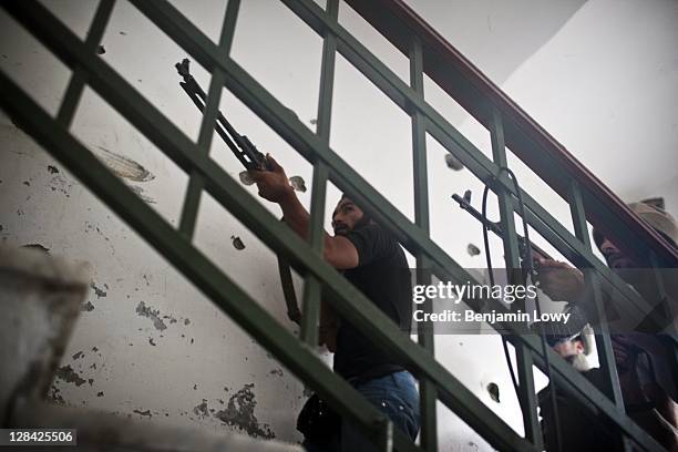 Two Libyan rebels run up a cramped stairway to fire their weapon at a Gaddafi loyalist sniper hiding out on the floor above in the Abu Salim...