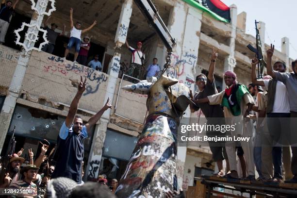 Libyans raise their arms in celebration as they tear down the infamous "hand crushing a plane" statue in Gaddafi's Bab al-Aziziyia compound on August...