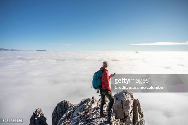 man hiker on top mountain using smart phone, blue clear sky over clouds - on top of clouds stock pictures, royalty-free photos & images