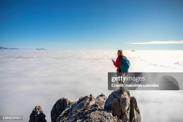 male hiker on top mountain using satellite phone, blue clear sky over clouds - tech summit stock pictures, royalty-free photos & images