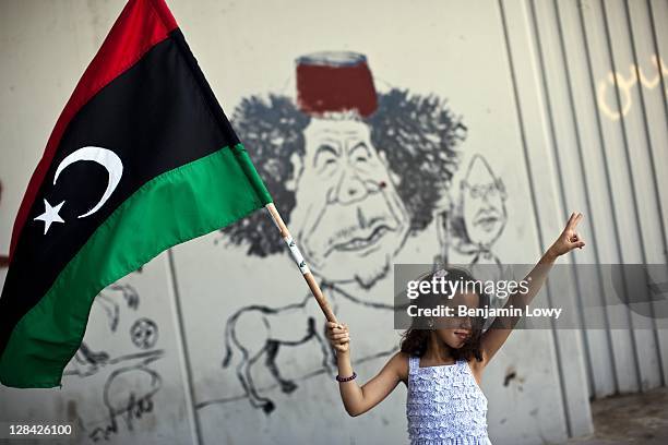 Young Libyan girl waves a flag in front of anti-Gaddafi graffiti scrawled on an underpass wall on August 29 2011 in Tripoli, Libya.