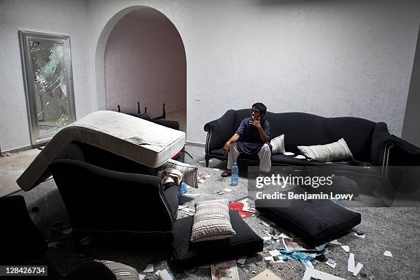 Libyan rebels sits on a couch and smokes a cigarette in the looted and NATO bombed home of former Libyan dictator Moammar Gaddafi's son Motasem, on...