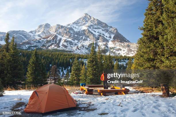 winter camping in mountains with caucasian man standing by fire - kananaskis stock pictures, royalty-free photos & images