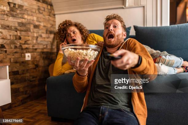 una joven pareja sorprendida viendo una película en casa. - lovers 2020 film fotografías e imágenes de stock