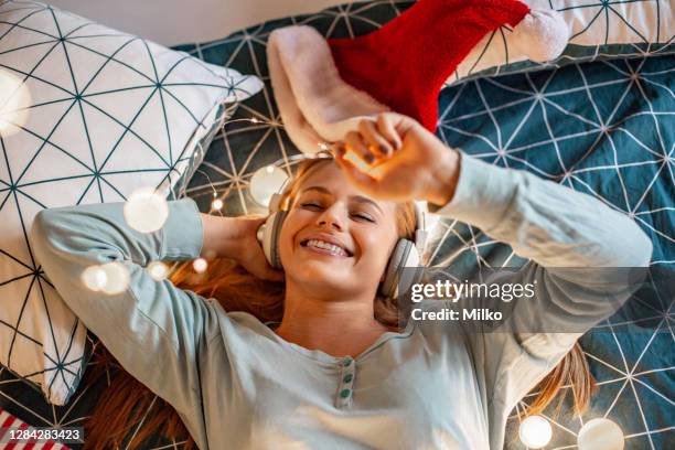 portrait of woman relaxing in bed and listening music during holiday season - christmas music listen stock pictures, royalty-free photos & images