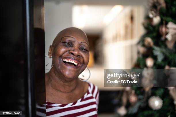 gelukkige hogere vrouw die huisdeur, kerstboom op de achtergrond opent - homeowners decorate their houses for christmas stockfoto's en -beelden