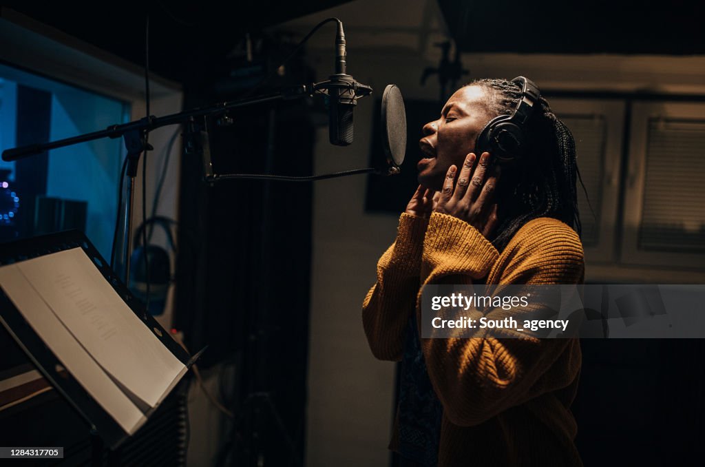 Black female singer singing into microphone in recording studio