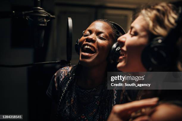 two female singers singing into a condenser microphone while recording a song in a professional studio - duet stock pictures, royalty-free photos & images