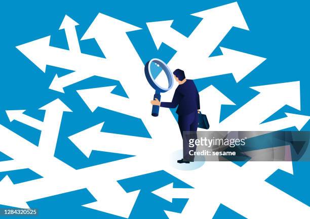 businessman holding a magnifying glass standing in a complicated arrow path observing and making a choice - choosing stock illustrations