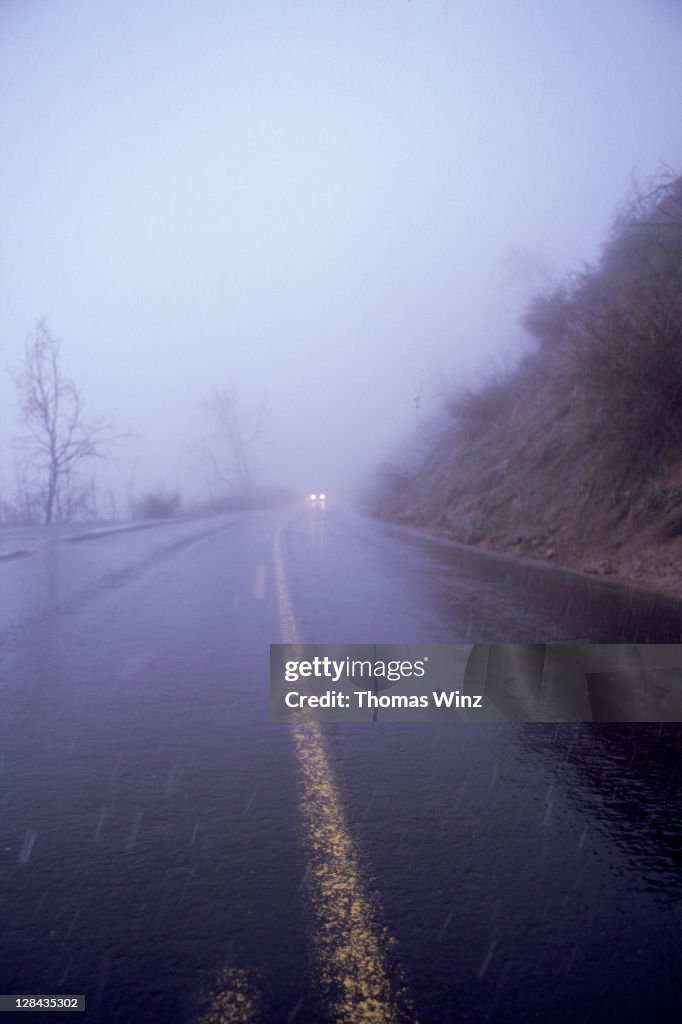 Car lights in fog and wet road from rain, ca