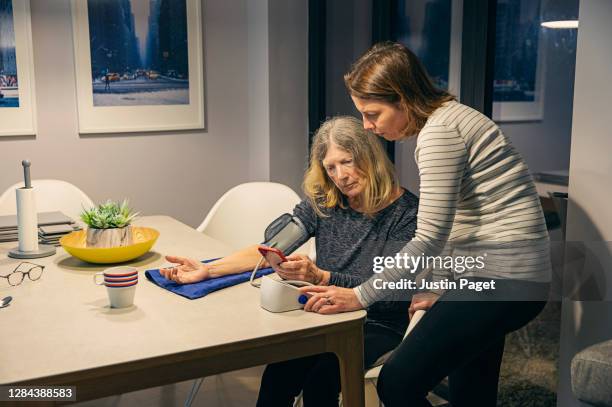 senior woman taking her blood pressure with daughter helping - cellphone cancer illness stock pictures, royalty-free photos & images